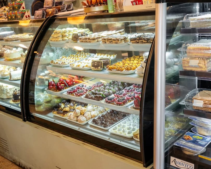 A brightly lit display case filled with various pastries, cakes, and chocolate-dipped fruits.
