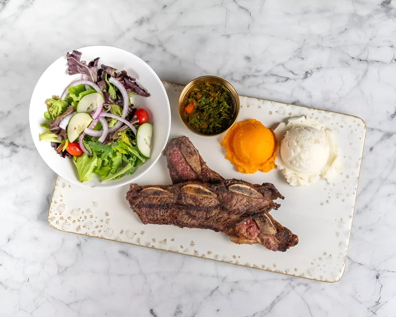 Grilled short ribs with a side salad, chimichurri, mashed sweet potatoes, and mashed potatoes.