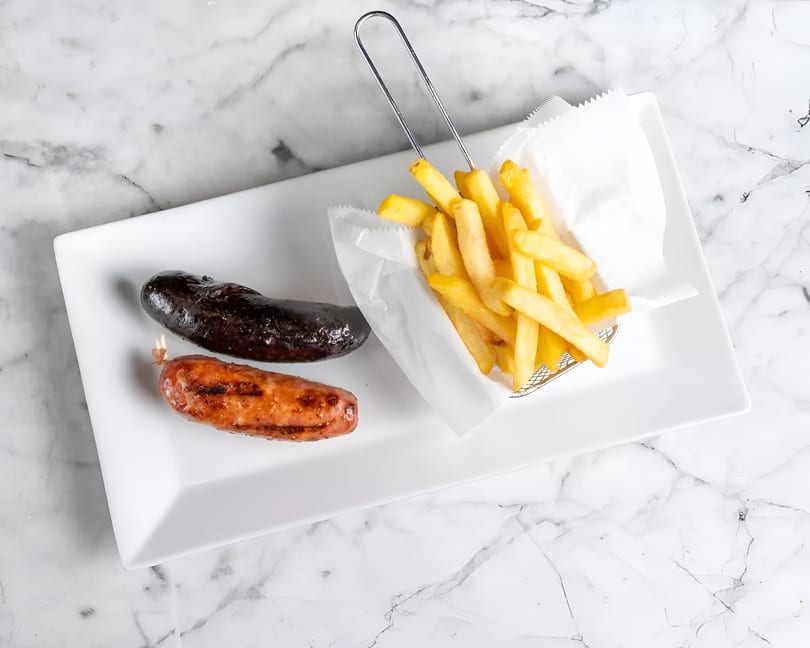 Two grilled sausages, one dark and one lighter, with a side of golden french fries.